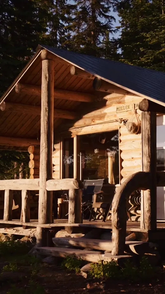A log cabin at Caverhill with a covered porch in evening light, a chair by the door