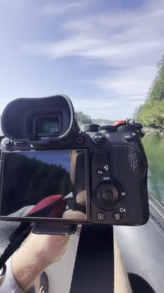 The Sony 200-600 on the A1 resting on the tube of an inflatable skiff, the strait and forested islands ahead