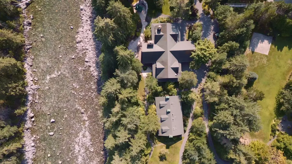 The lodge from directly above, three cabin roofs among the trees beside a wide grey riverbed