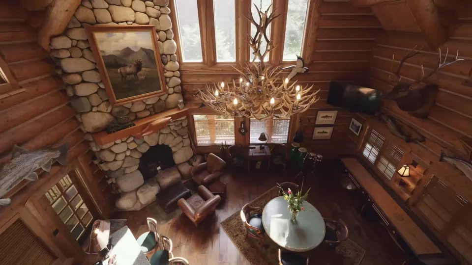 The great room from above, an antler chandelier over a stone fireplace and leather chairs