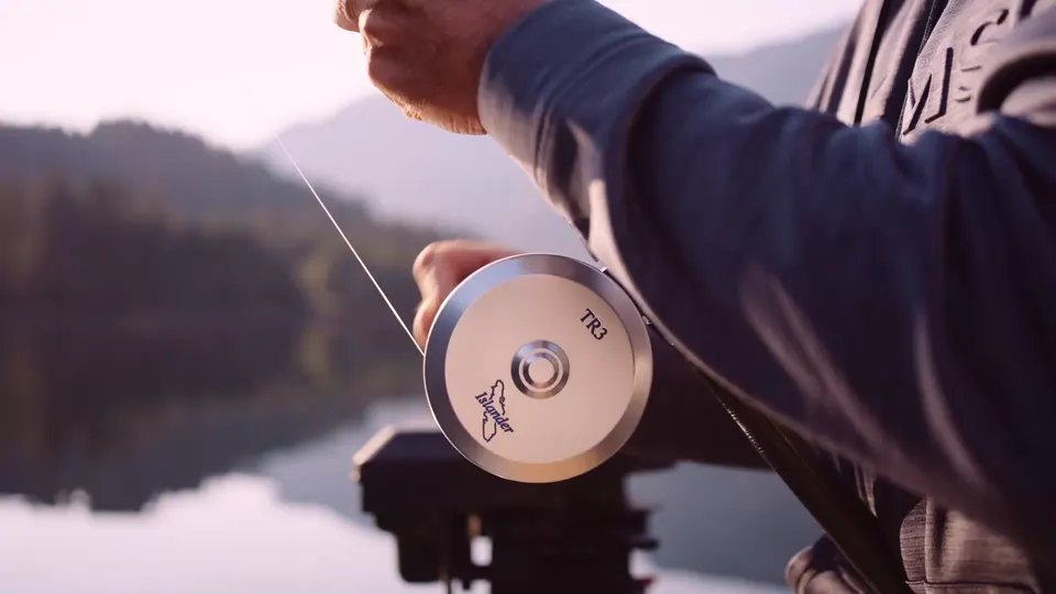 Close on a fly reel and a line being stripped in, the inlet soft behind it