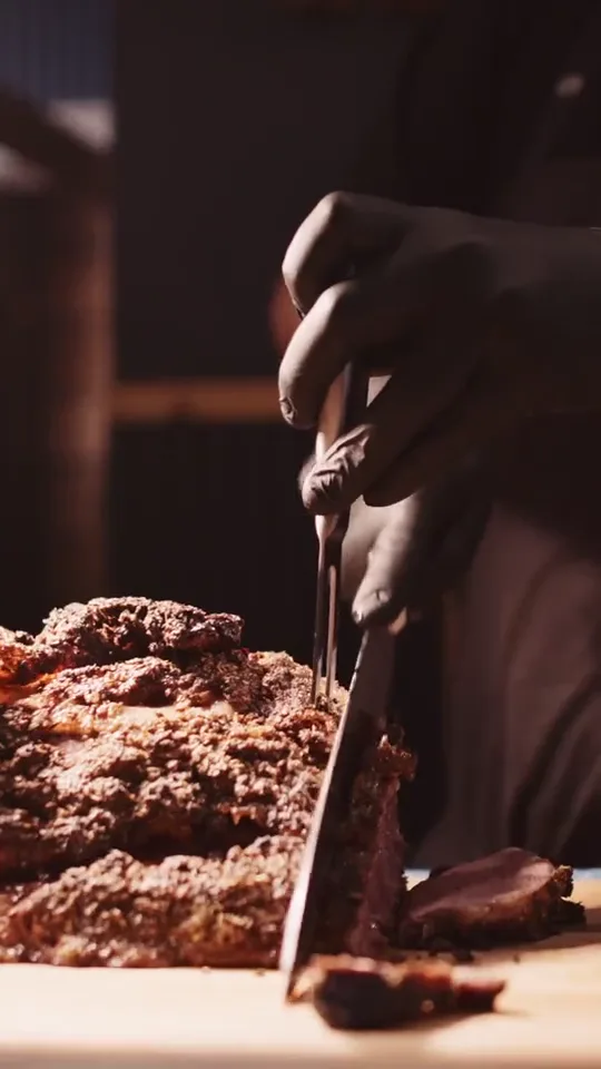 Gloved hands slicing a dark seared crust on a board in the lodge kitchen