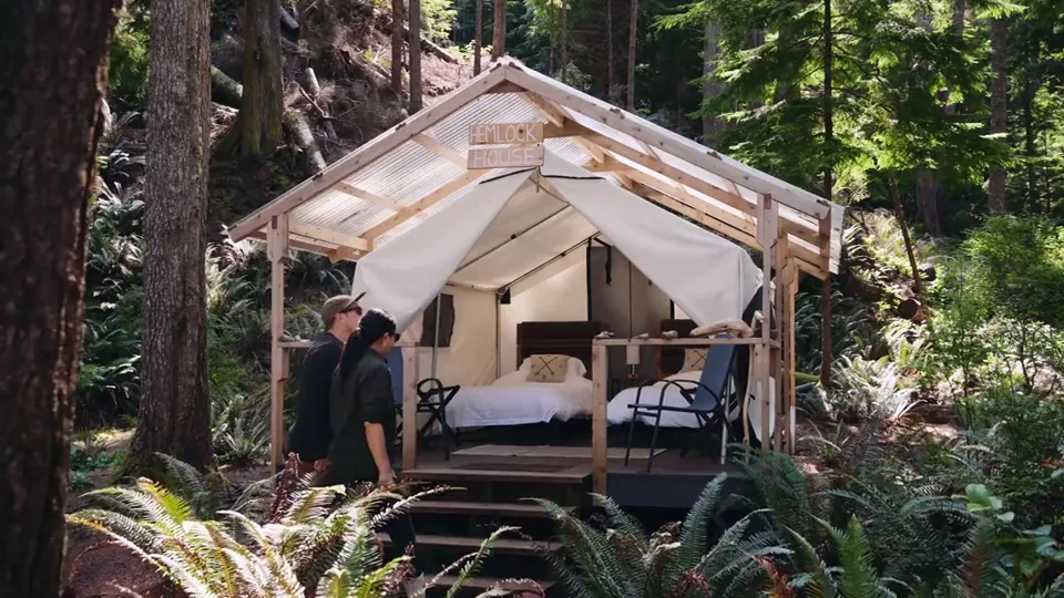 Hemlock House, a canvas-walled cabin on a timber frame in the rainforest, two guests at its door