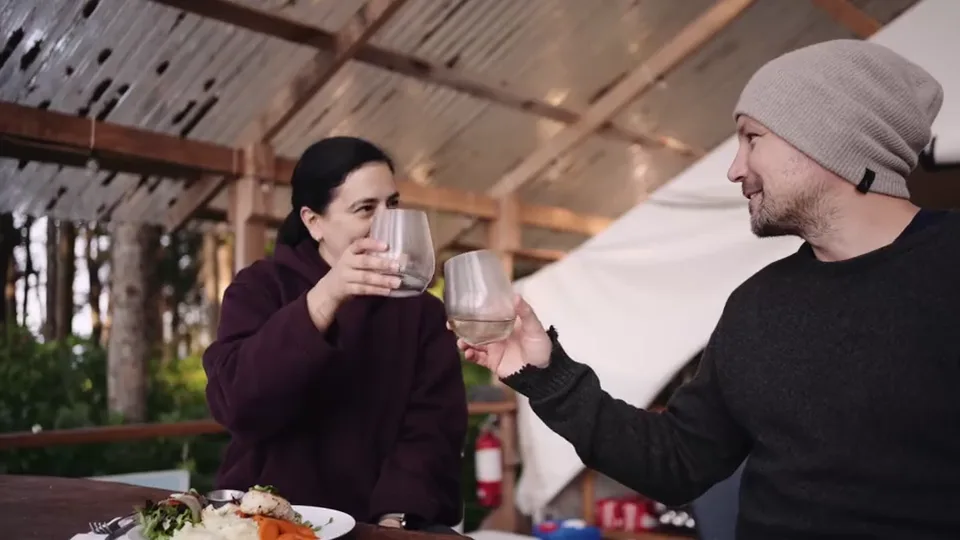 Two guests raising glasses across the dinner table under the canvas dining shelter