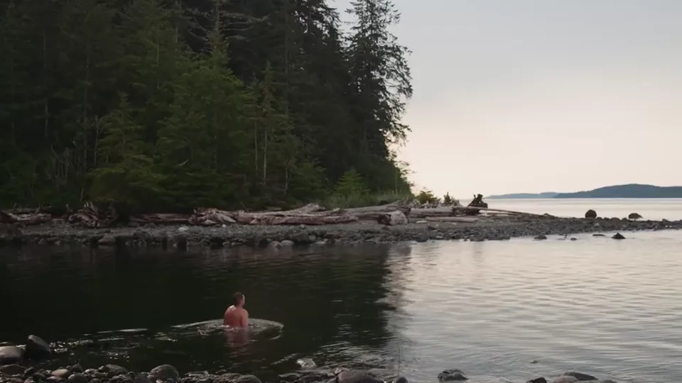 The strait flat and pink at dusk, a swimmer in the water off the pebble beach