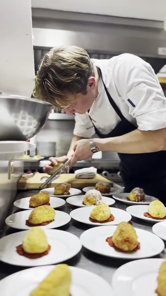 A chef in whites plating a row of dishes on the pass in the lodge kitchen