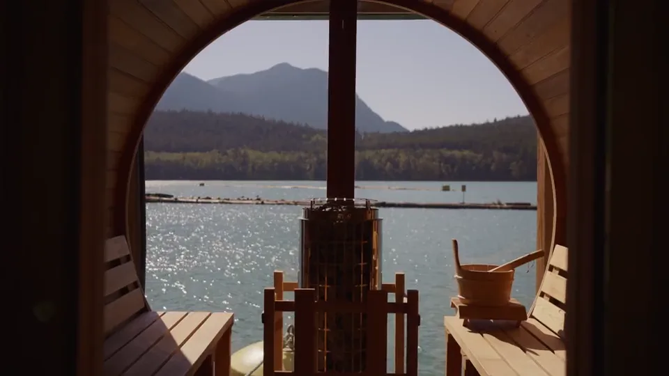 Looking out through the barrel sauna's round window from inside: the stove, the bucket, the dock and the inlet in daylight